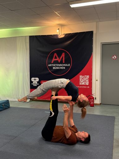 Zwei Akrobaten führen einen Partnertrick auf einer Matte aus.