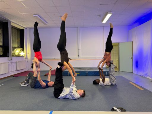 Sechs Akrobaten in einer Turnhalle, verschiedene Posen, einige stehen auf den Händen.
